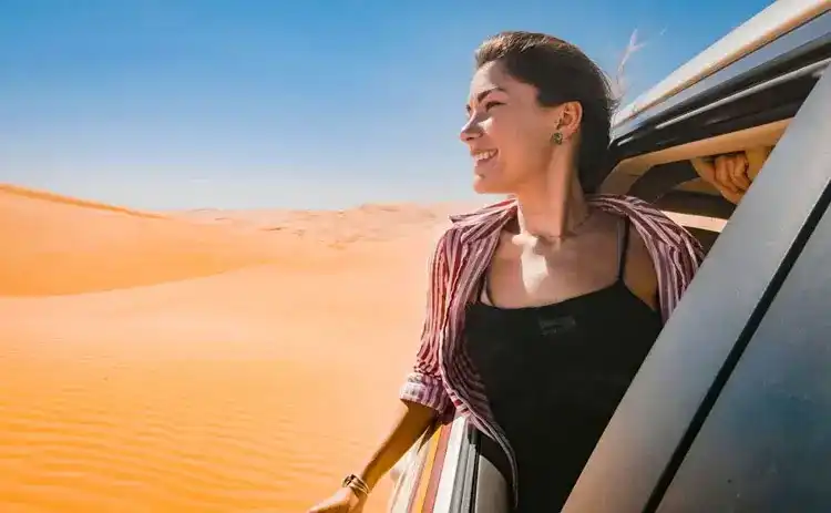 Une voyageuse souriante penchée à la fenêtre d'un 4x4 dans le désert
