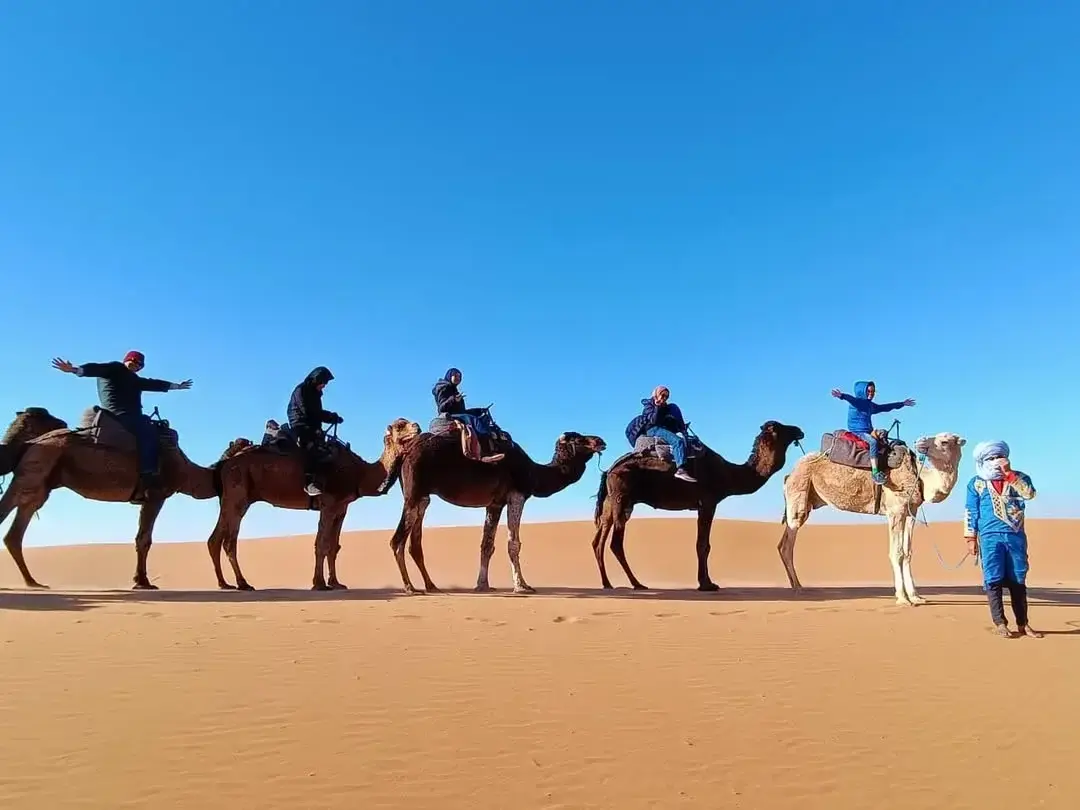 Reisende verschiedenen Alters bei einem Kamelritt in den Dünen von Merzouga, geführt von einem einheimischen Guide