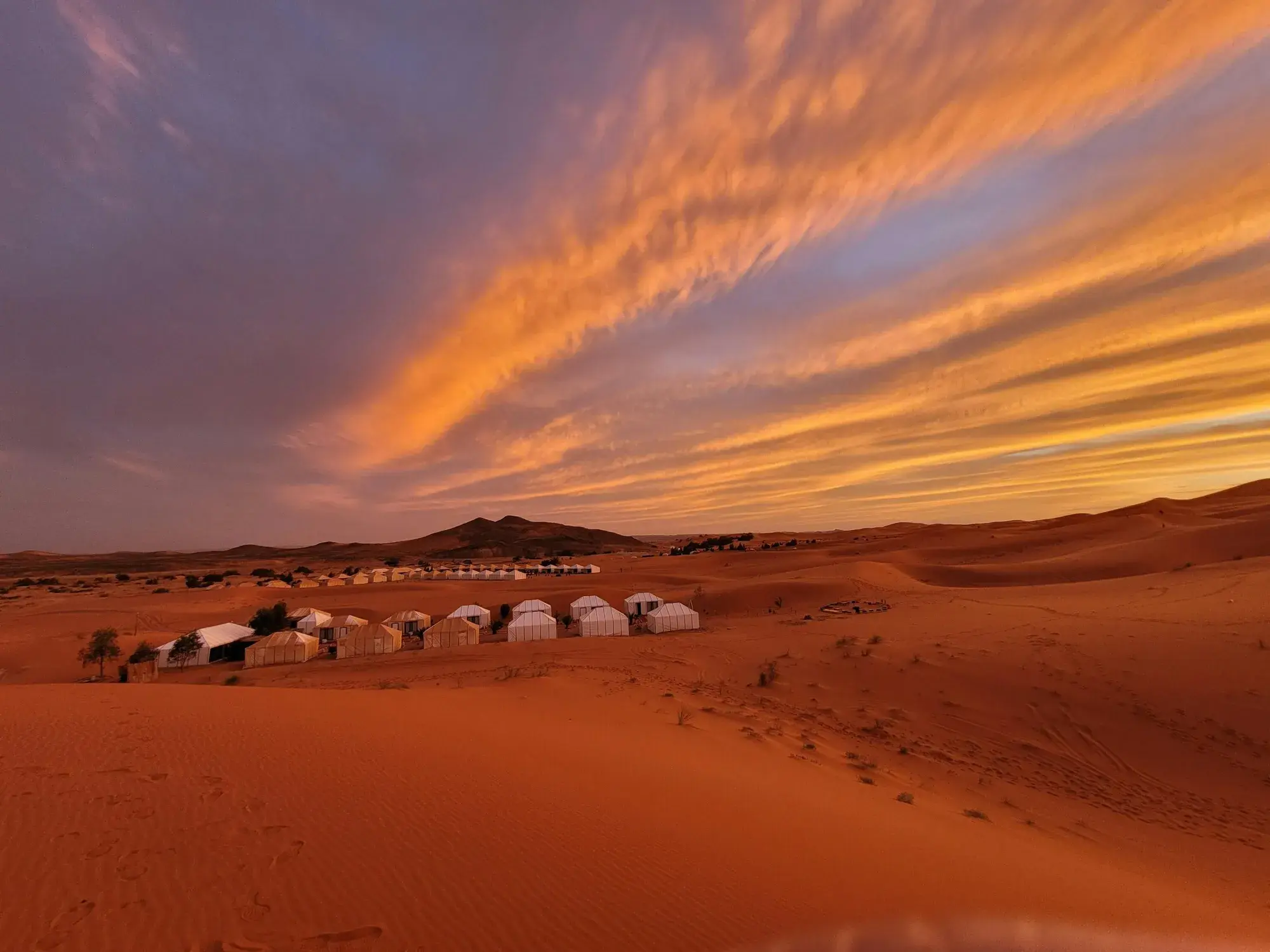 Weiße Zelte eines Wüstencamps zwischen den Dünen des Erg Chebbi bei Sonnenuntergang