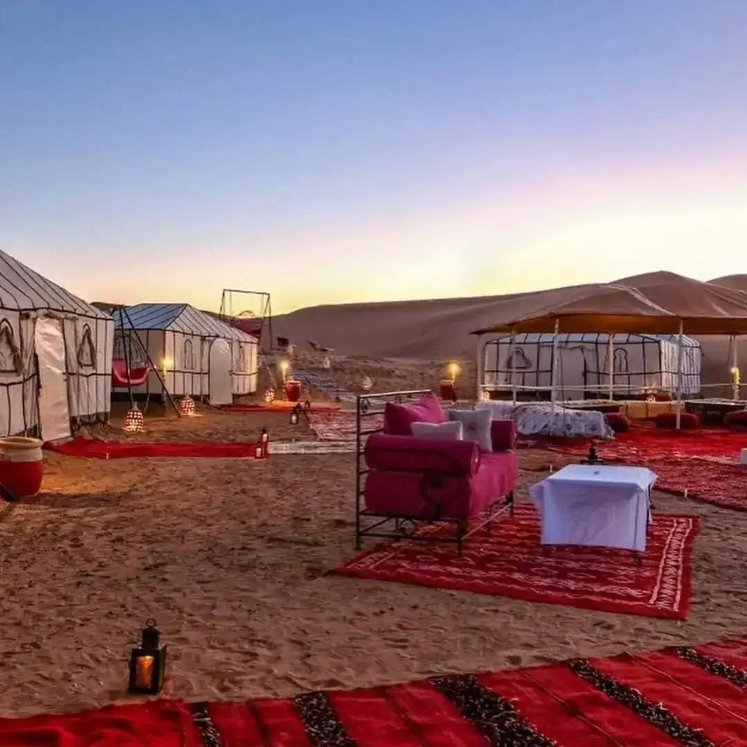 Tentes blanches, lanternes et tapis rouges dans un campement au crépuscule