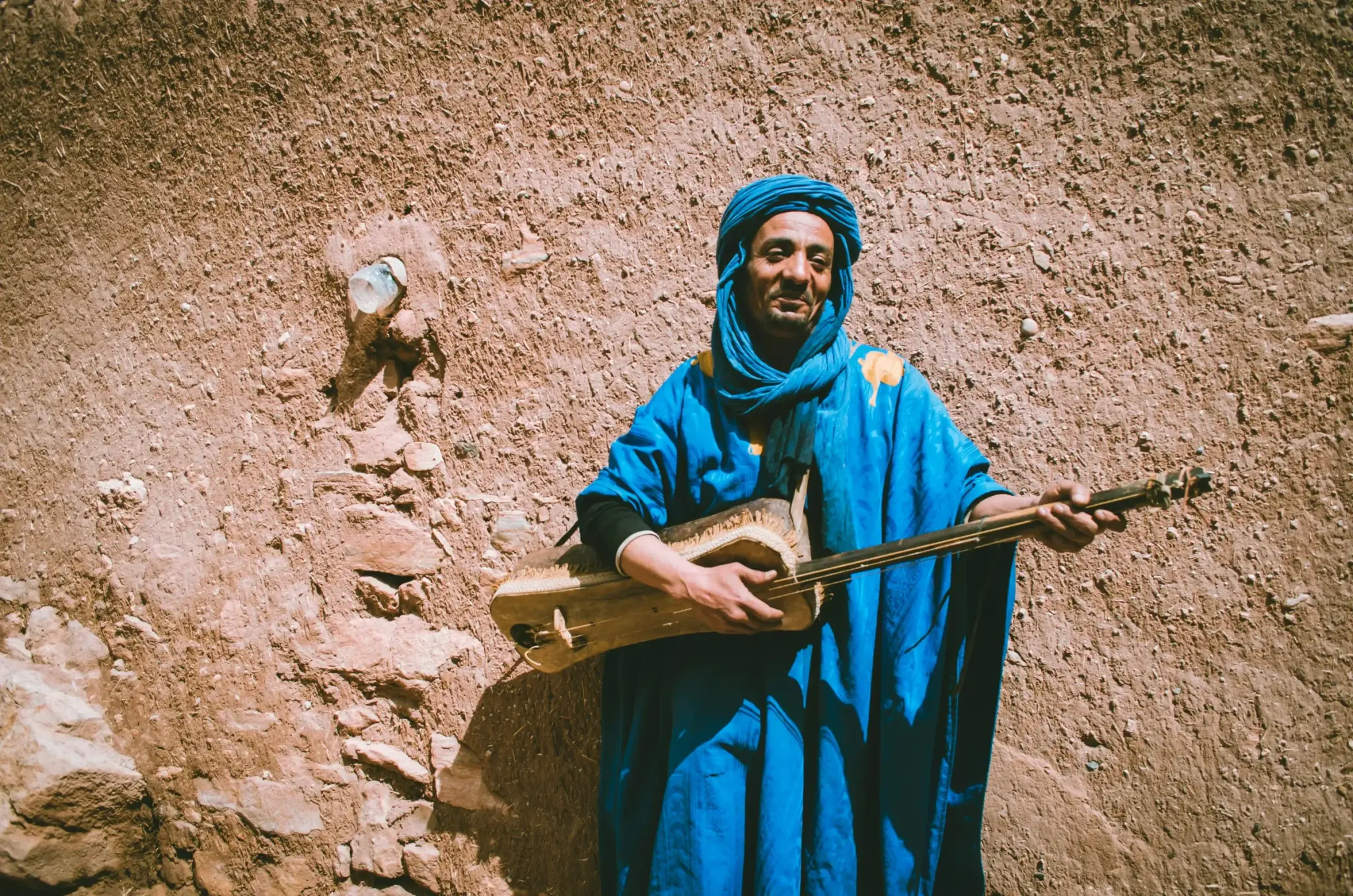 Ein Musiker in blauem Gewand und Turban spielt ein traditionelles Saiteninstrument
