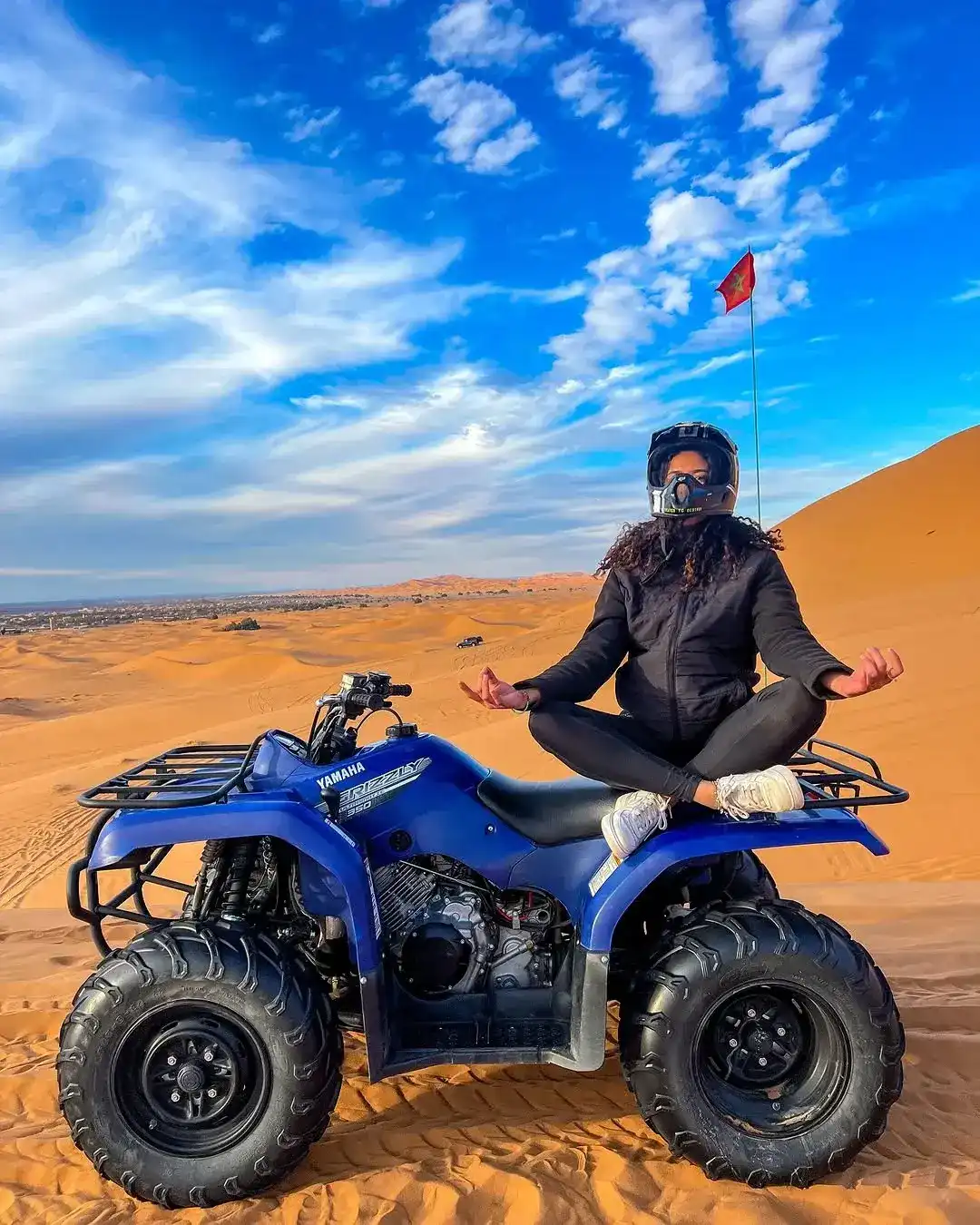 A rider in a helmet sitting on a quad bike at the top of a dune