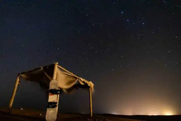 Uma prancha de sandboard encostada a um abrigo de sombra sob um céu cheio de estrelas no deserto de Merzouga